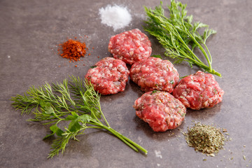 Raw minced meat patties with spices, seasonings and herbs on a marble background.View from above.