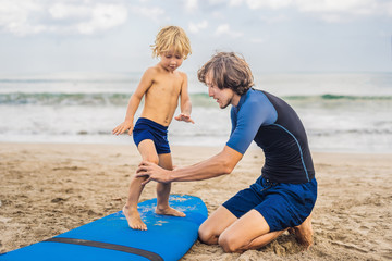 Father or instructor teaching his 4 year old son how to surf in the sea on vacation or holiday....