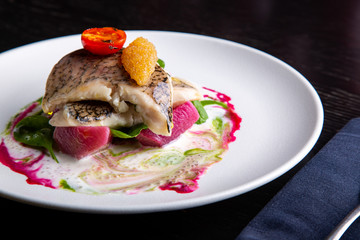 delicious restaurant dish of white fish, pike, sea bass with vegetables under the sauce in restaurant background. Healthy exclusive food on big white plate closeup
