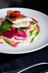 delicious restaurant dish of white fish, pike, sea bass with vegetables under the sauce in restaurant background. Healthy exclusive food on big white plate closeup