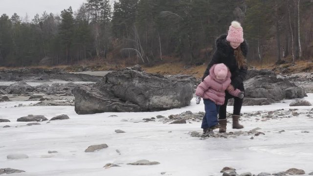 small laughing girl falls on slippery ice and her sister helps her get on feet