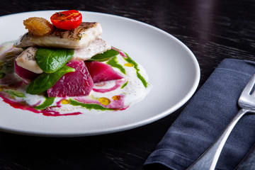 delicious restaurant dish of white fish, pike, sea bass with vegetables under the sauce in restaurant background. Healthy exclusive food on big white plate closeup
