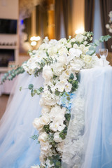 Wedding presidium in restaurant, free space. Wedding banquet table for newlyweds with flowers, greenery, pink cloth and bulbs. Lush floral arrangement on wedding table. Luxury wedding decorations
