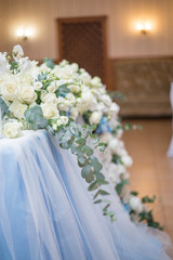 Wedding presidium in restaurant, free space. Wedding banquet table for newlyweds with flowers, greenery, pink cloth and bulbs. Lush floral arrangement on wedding table. Luxury wedding decorations