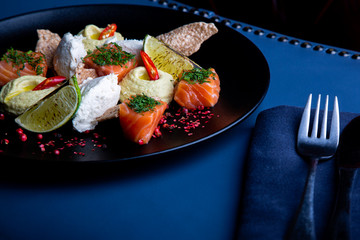 delicious salmon with pate and hummus in restaurant background. Healthy exclusive food on big black platter closeup