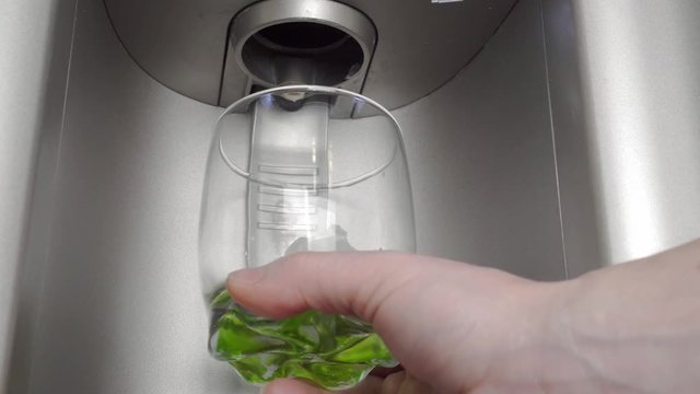 A woman's hand picks up ice cubes in a glass from the dispenser of a home refrigerator.
