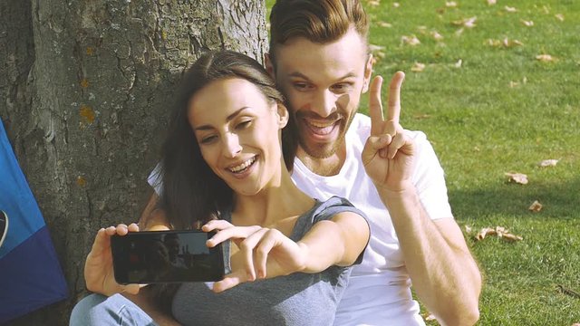 Happy couple taking a picture of themselves with a smartphone on a green lawn. Slow motion.