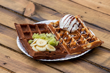 Belgian waffle with banana and kiwi and chocolate wafer with ice cream ball and chocolate topping.