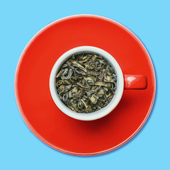 Green tea leaves in red ceramic cup isolated on blue studio background.