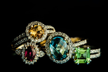 Four shiny golder rings with precious gems isolated on black.