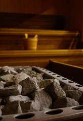 Wooden Bathhouse with a heating pot filled with stones, close up. Wooden sauna interior with equipment, coals, ladle, bucket.