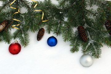 Green spruce branches with cones and colorful toys are lying on the snow