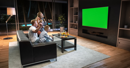 A family is watching a TV and celebrating some joyful moment, sitting on the couch in the living room.