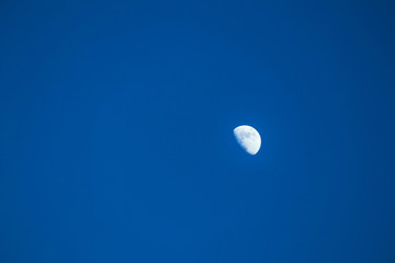 A half of white bright moon on a clear blue sky, calm beautiful view.
