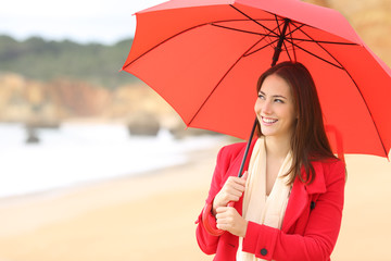 Happy woman in red holds an umbrella on the beach