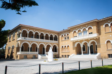Fototapeta na wymiar Archbishop's famous palace in Cyprus - a three-story building made in neo-Byzantine style. The decoration is high arches, elegant stucco and large windows. Nearby is the bronze statue of Makarios III