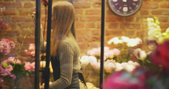 Caucasian woman taking carnation from tloral refrigerator,