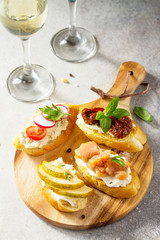 Italian Antipasti snacks set for Wine. Brushetta with Soft Cheese, Pear, Radish, Salmon and Dried Tomatoes on a light stone background.