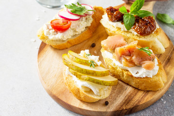 Italian Antipasti snacks set close-up for Wine. Brushetta with Soft Cheese, Pear, Radish, Salmon and Dried Tomatoes on a light stone background.