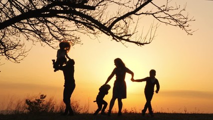 Silhouettes of family spending time together in the meadow near during sunset