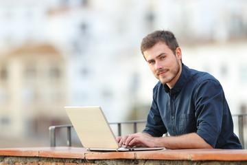 Man using a laptop and looking at camera in a balcony