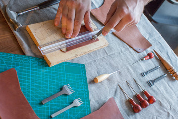 Hands of the master. Marking and slicing red leather for making bags, purses or shoes.