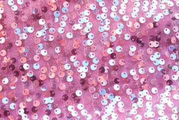 pink textured background of shiny round multicolored iridescent sequins sewn on fabric for a trendy...