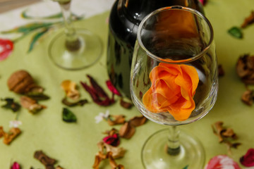 Romantic composition with wine glass, roses and bottle of wine. Candle light and dry leaves of flower on the table.