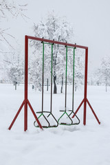 Snow landscape. Empty kids metal swing in the park