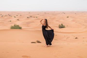 Portrait of beautiful young woman in long fluttering black dress posing outdoor at sandy desert