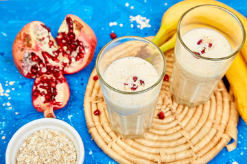 Smoothie with oat or oatmeal, banana and pomegranate on blue background.