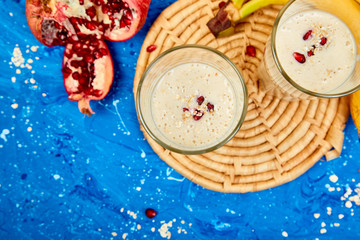 Smoothie with oat or oatmeal, banana and pomegranate on blue background.