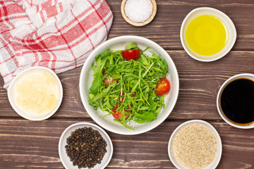 Mixed arugula leaves and sliced cherry tomatoes. recipe step by step arugula salad with a tea towel flatlay on brown wood