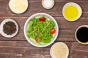 Mixed arugula leaves and sliced cherry tomatoes. recipe step by step arugula salad in a grey ceramic bowl flatlay on brown wood