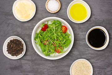 Mixed arugula leaves and sliced cherry tomatoes. recipe step by step arugula salad in a grey ceramic bowl flatlay on grey stone