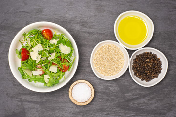 Adding ingredients step. recipe step by step arugula salad in a grey ceramic bowl flatlay on grey stone