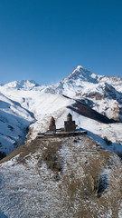 Aerial photo of the lonely historic Gergeti Trinity Church in Kazbegi, Georgia. It is winter.There are snowy mountains around the church and clear blue sky. Georgian ortodox architecture, culture.