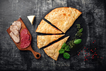 Traditional Italian pizza calzone with ingredients on a stone and dark wooden scratched background