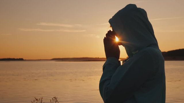 Silhouette of a woman praying at sunset by the lake