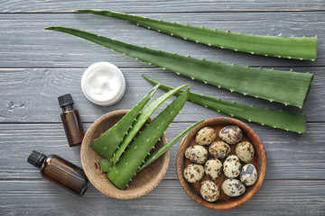 Fresh aloe leaves with cosmetic products and eggs on wooden table