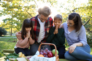 Family praying before meal in park