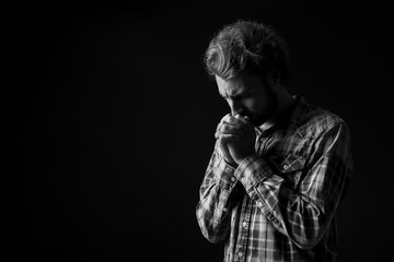 Black and white portrait of young praying man on dark background