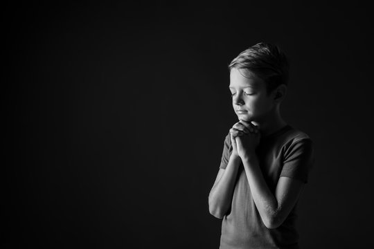 Black and white portrait of praying boy on dark background