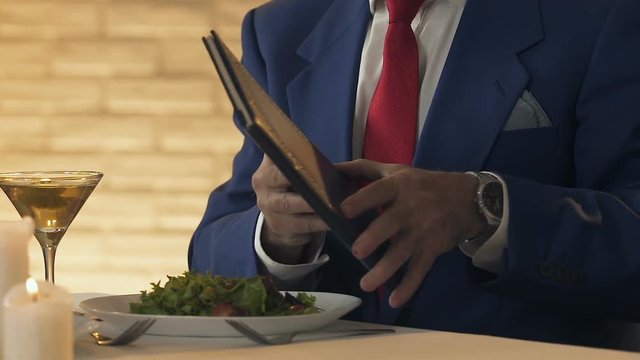 Waiter giving menu or bill to wealthy man, business lunch, restaurant service