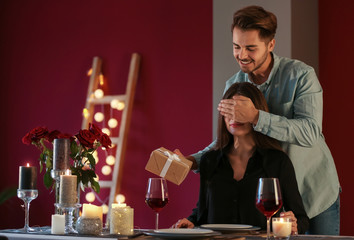 Man with gift box covering eyes of his girlfriend in restaurant