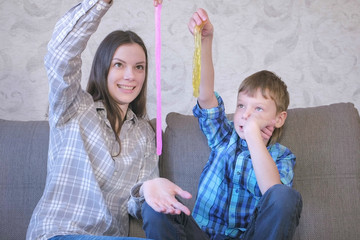 Happy mom and son are playing with slime sitting on the sofa. Stretching slime.
