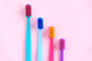 Four Colorful toothbrushes with selective focus on pink background. Toothbrush for personal routine morning  hygiene on neutral blurred backdrop. Dental plastic tool with empty space for image or text