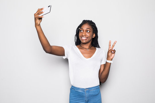 Smiling attractive african woman showing peace gesture and taking a selfie while standing isolated over gray background
