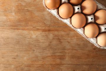 Carton box with raw chicken eggs on wooden table