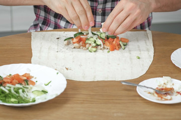 Man is cooking shawarma on the kitchen table at home. Pita, vegetables and green onion with sauce and mayonnaise. Close-up hands.